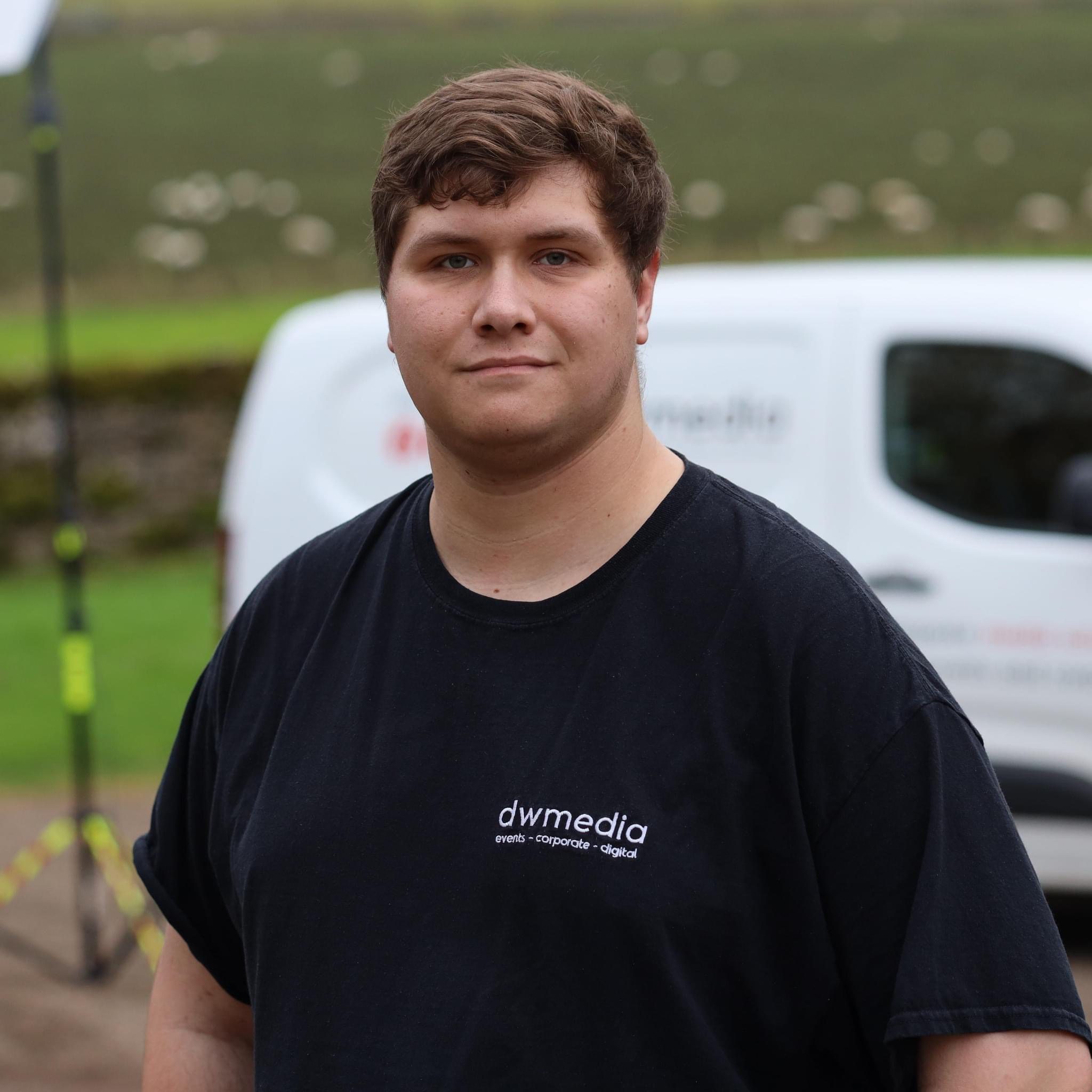 Daniel Wilkinson in a dwmedia shirt in front of a dwmedia van on a rural event site